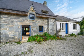 Une maison en pierre avec une allée en gravier, un banc en bois et un petit jardin.