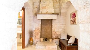 Una habitación de paredes de piedra con chimenea, un banco de madera y un cuadro en la pared.