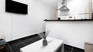 Ett modernt kök med en platt-TV, en rostfri köksfläkt och en vit bänkskiva.