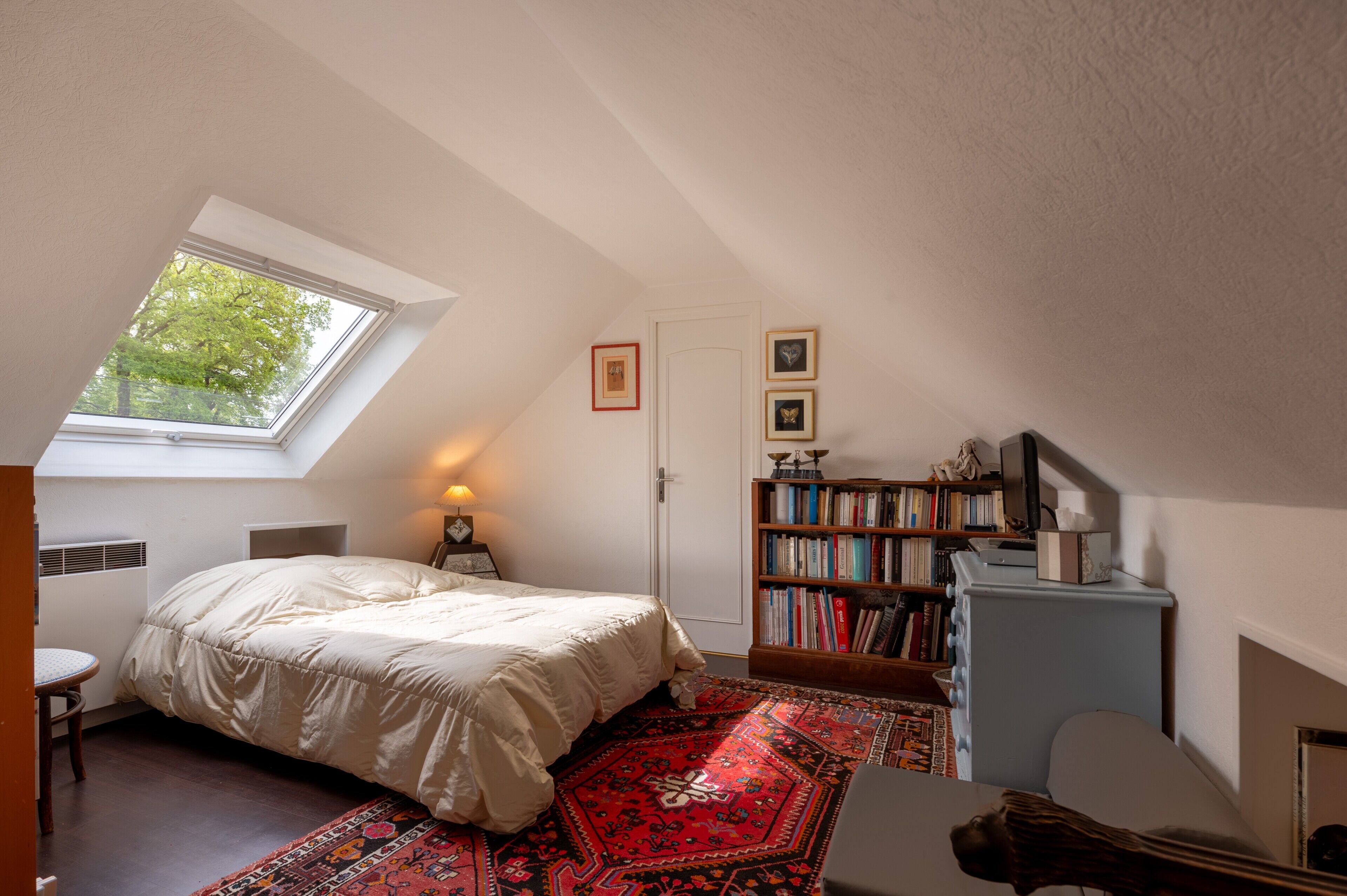 A bedroom with a skylight, a bed, a bookshelf, and a desk.
