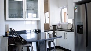 A modern kitchen with white cabinets, a stainless steel refrigerator, and a glass-fronted cabinet displaying wine glasses. - Mmaset Houses 3-bedrooms (Gaborone)