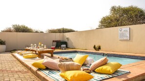 A poolside area with a table set for a meal, lounge chairs, and a sign with pool rules. - Mmaset Houses 3-bedrooms (Gaborone)