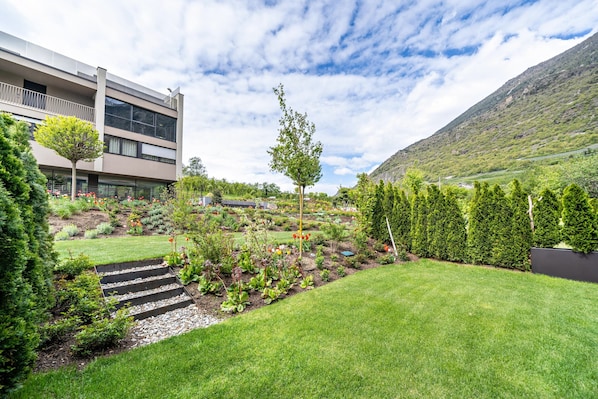 A modern building with a garden featuring a variety of plants and a small tree.
