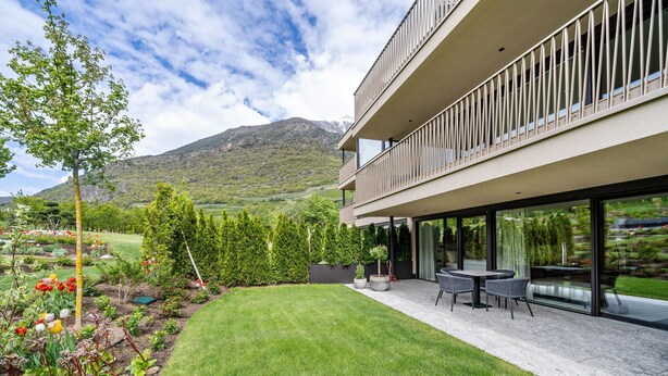 Een modern gebouw met een balkon, een verzorgd gazon en een bergachtige achtergrond.