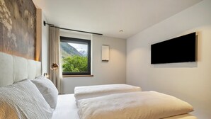 Een moderne hotelkamer met een bed, een televisie en een raam met uitzicht op de bergen.
