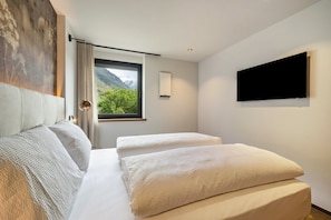 Una habitación de hotel moderna con cama, televisor y ventana con vistas a la montaña.