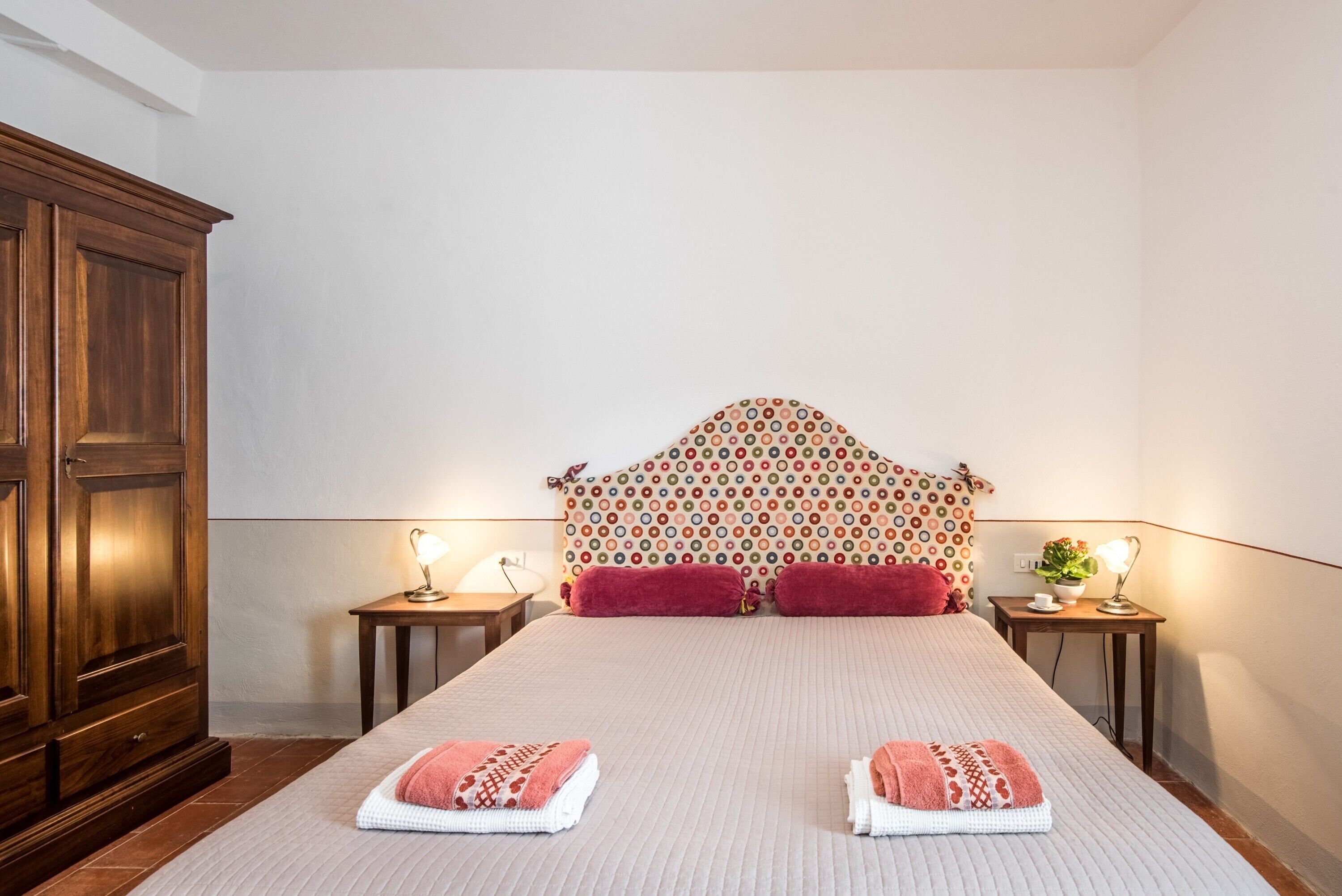 Un lit bien fait, avec deux oreillers, une armoire en bois et deux tables de chevet avec des lampes.