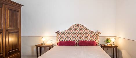 Un lit bien fait, avec deux oreillers, une armoire en bois et deux tables de chevet avec des lampes.
