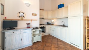 A kitchen with white cabinets, a stove, a microwave, and a television on a cabinet.