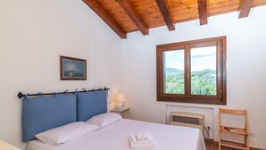 A bedroom with a bed, a nightstand, a window with a view, and a wooden ceiling.