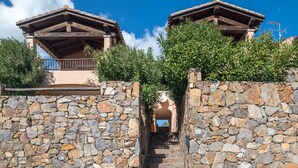 A stone wall with a staircase leading to a building with a wooden roof and balcony.