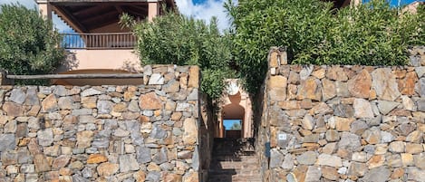 A stone wall with a staircase leading to a building with a wooden roof and balcony.