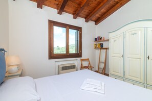 Un dormitorio con cama, ventana, radiador, estantería y armario.