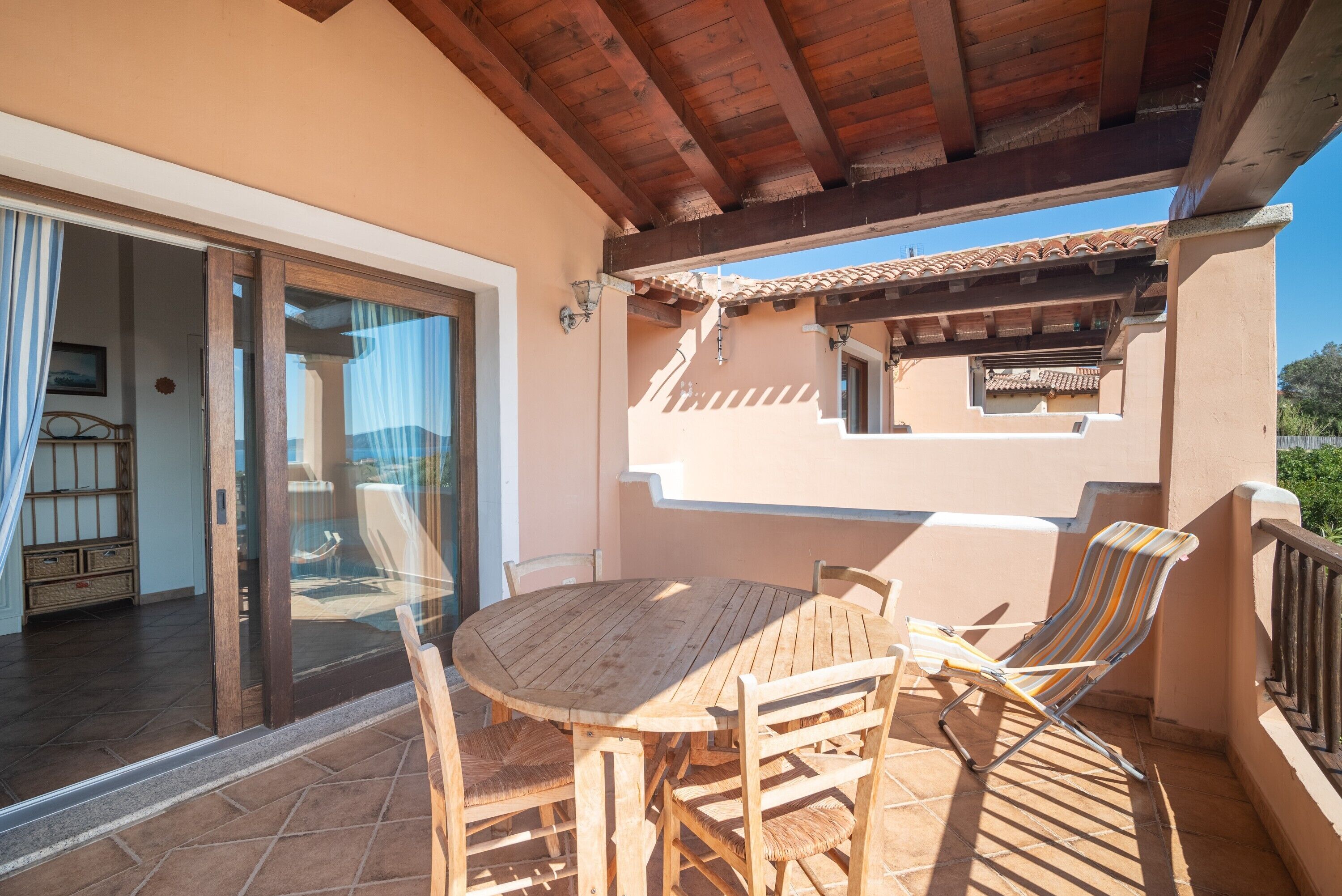A wooden table and chairs on a balcony with a view of a building and a door leading to an interior space.