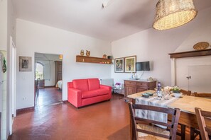 A spacious living area with a red sofa, a dining table, and a television mounted on the wall.