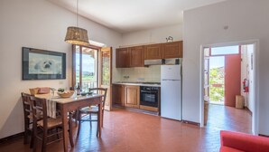 Une cuisine avec des meubles en bois, une table à manger avec des chaises, un luminaire suspendu et un tableau encadré au mur.