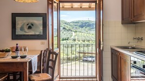 Une cuisine avec un coin repas, un tableau encadré représentant un chien et une vue sur un paysage verdoyant par une porte ouverte.