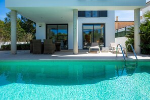 Un espace piscine extérieur moderne, doté de chaises longues et d’un coin salon abrité.