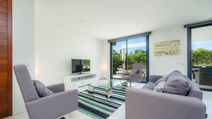 A modern living room with a glass coffee table, two grey sofas, a flat-screen TV, and a large sliding glass door leading to an outdoor area. - Villa 'Oasis N'Aguait' with Private Pool, Wi-Fi and Air Conditioning (Cala Rajada)