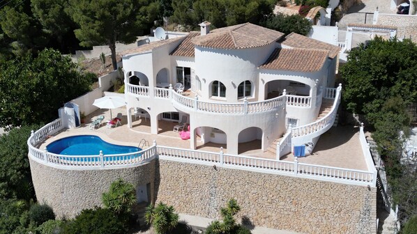 A multi-story villa with a swimming pool, outdoor seating, and a stone retaining wall.