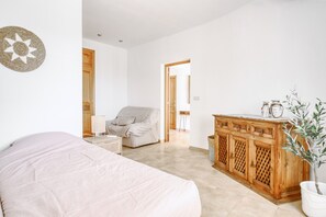 A bedroom with a bed, a chair, a wooden cabinet, and a potted plant.