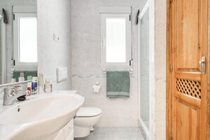 A bathroom with a large sink, toilet, and two windows.