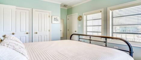 A bedroom with a bed, white doors, and windows with blinds.
