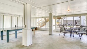 A spacious, open-plan area with a long table and chairs, large windows, and a staircase in the background. - The Salty Point....a waterfront fishing cottage with kayaks, ping pong and more! (Franklin)