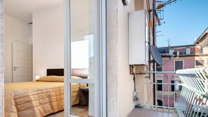 Une chambre à coucher avec un lit, une porte-fenêtre coulissante et un balcon doté d’une rambarde en métal.