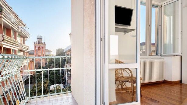 Un balcon avec vue sur les immeubles, une chaise à l’intérieur et un téléviseur fixé au mur.