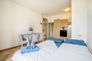 Une chambre avec un lit, une petite table avec des chaises, un coin cuisine et une porte.
