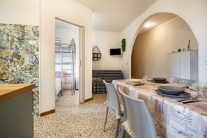 A kitchen with a dining table set for four, a sofa, and a TV mounted on the wall.