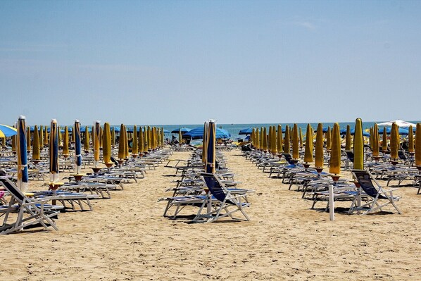 A beach with rows of sun loungers and umbrellas.