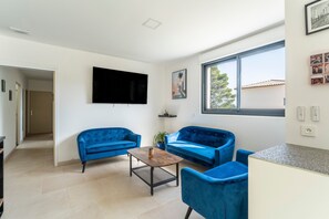 Una sala de estar con dos sofás azules, una mesa de centro, un televisor de pantalla plana y un ventanal grande.
