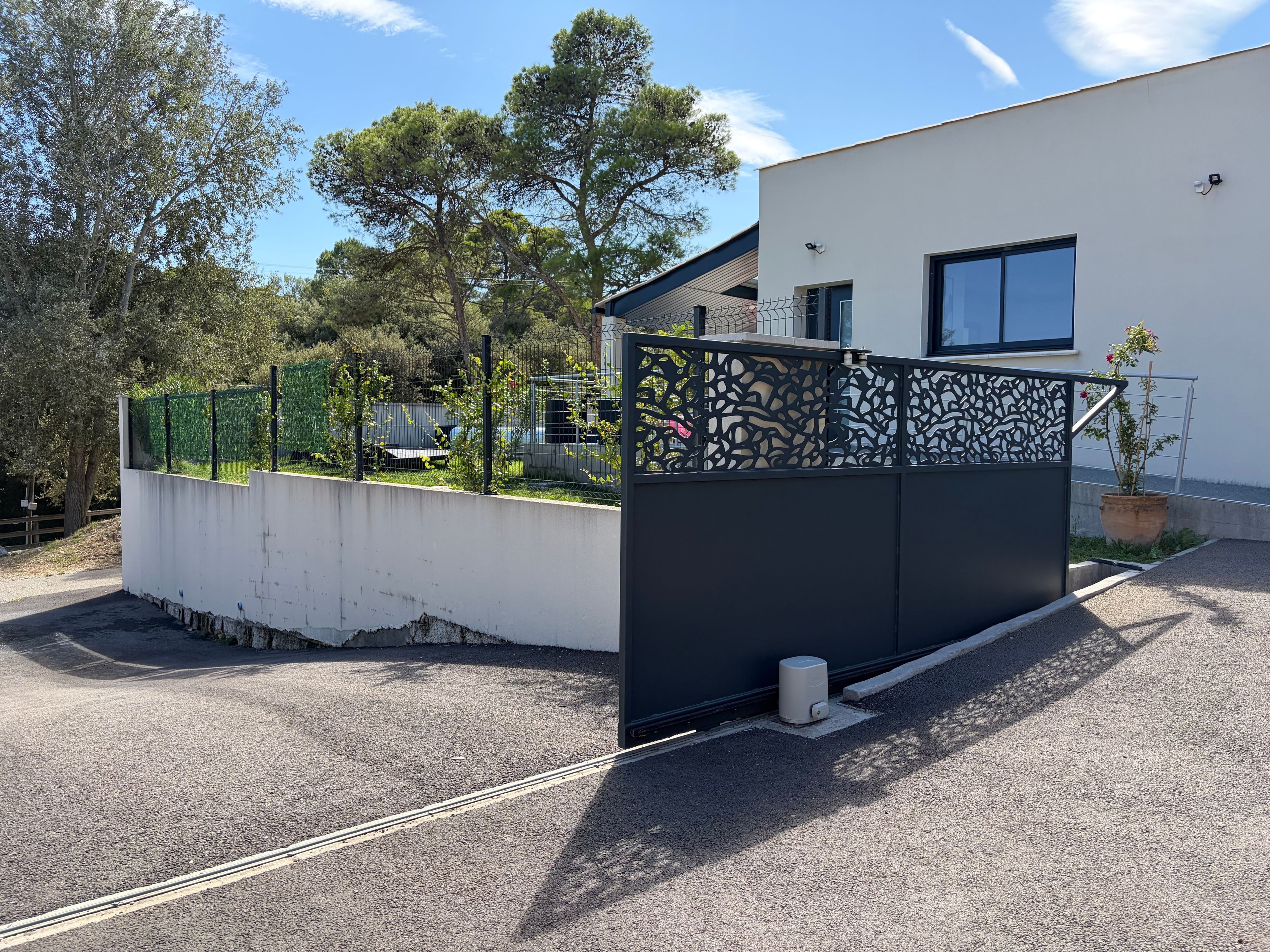 Un bâtiment moderne à l’extérieur blanc, agrémenté d’une clôture noire décorative et d’une plante en pot.