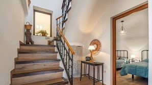 Una scala in legno con ringhiera, un tavolino con una lampada e un letto con coperta verde.