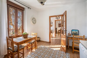Huoneessa on puinen ruokapöytä, tuoleja, kuviollinen matto, kello ja näkymä avoimesta ovesta.