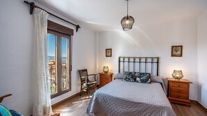 Una camera da letto con un grande letto, due comodini con lampade, una sedia, una finestra con tende e vista sull'esterno.