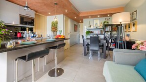A modern kitchen with a bar area, dining space, and a living area with a sofa and a lamp. - Apartment 'Des Vacances De Rêve À Mandelieu' with Shared Pool and Air Conditioning (Mandelieu-la-Napoule)