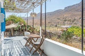 Un balcón con mesa y sillas, una lámpara colgante y vistas a un paisaje montañoso.