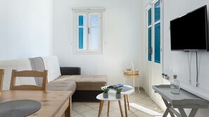 A modern living room with a sofa, a dining table, a TV, and a window with blue shutters.