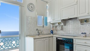 A kitchen with white cabinets, a clock, a window, and a view of the sea.