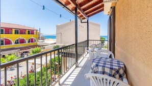 A balcony with white chairs and a table, overlooking a beach and a building with a red facade. - Apartment 'Mires House  11' with Sea View, Wi-Fi and Air Conditioning (Corfu)