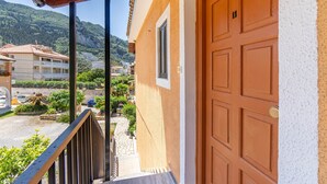 A building with a wooden door, a balcony with a metal railing, and a view of a mountainous area. - Apartment 'Mires House  11' with Sea View, Wi-Fi and Air Conditioning (Corfu)
