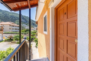 A building with a wooden door, a balcony with a metal railing, and a view of a mountainous area.
