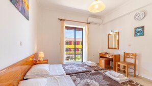A hotel room with two beds, a desk, a chair, a mirror, and a view of a colorful building through the window. - Apartment 'Mires House  11' with Sea View, Wi-Fi and Air Conditioning (Corfu)