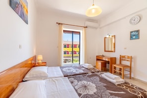 A hotel room with two beds, a desk, a chair, a mirror, and a view of a colorful building through the window.