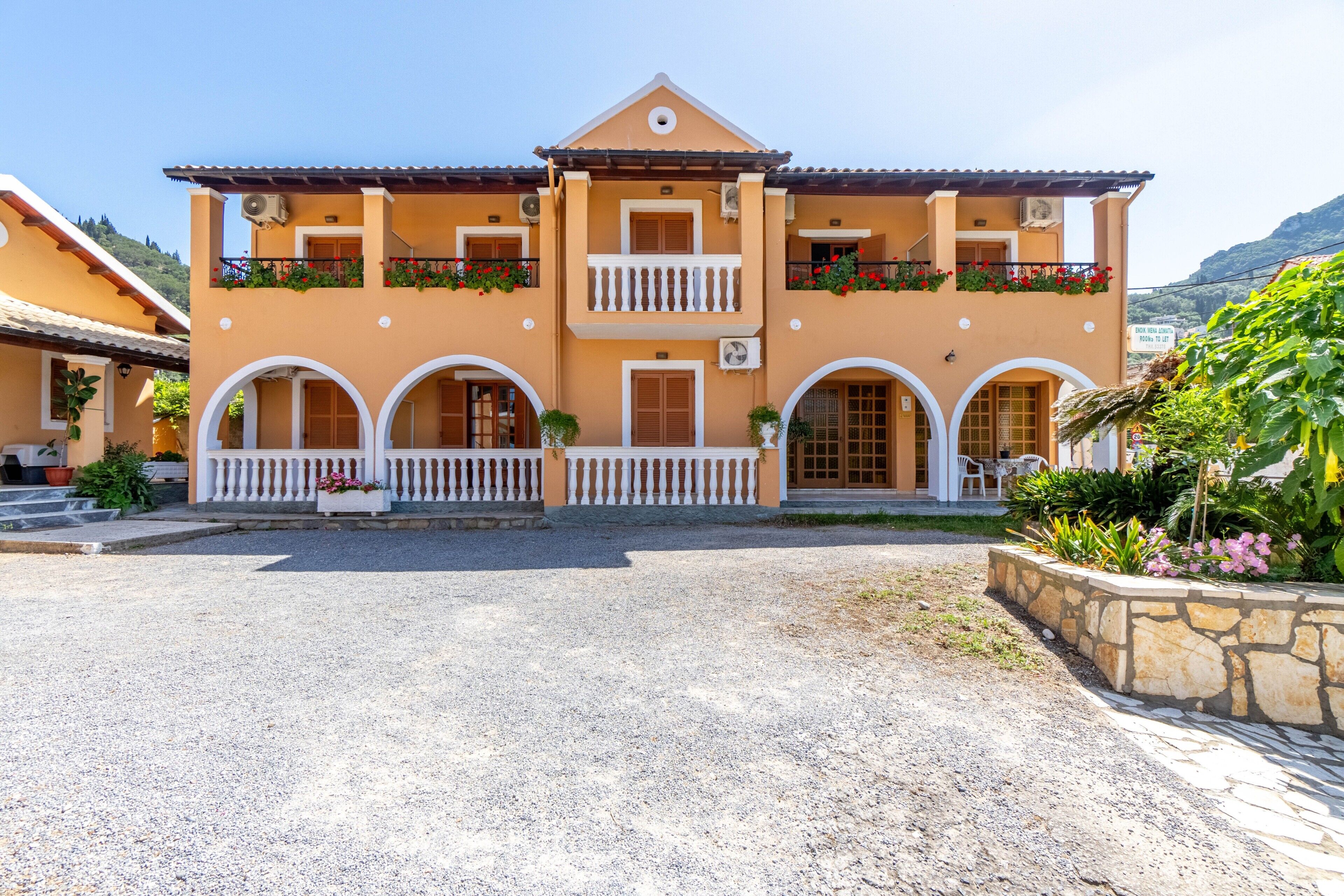 A two-story building with a balcony, a stone wall, and a gravel driveway.