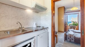Une cuisine compacte équipée d’un évier, d’une cuisinière et donnant sur un balcon avec coin salon extérieur.