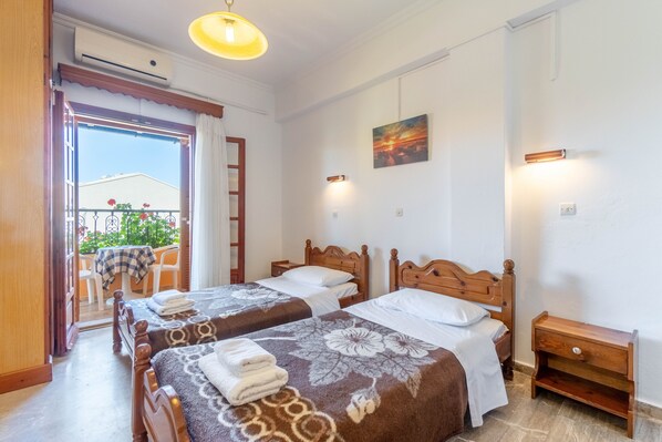 Une chambre d’hôtel avec deux lits en bois, un balcon avec vue, une table de chevet en bois et un tableau au mur.
